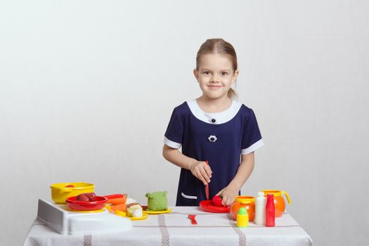 Five year old girl playing in a children's mistress dishes at a table covered with a cloth