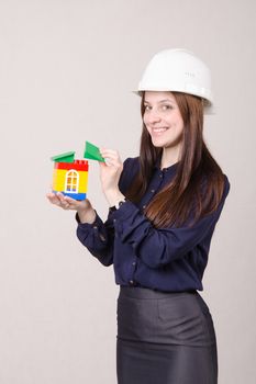 Young woman builder in helmet with a house worth in the hands of