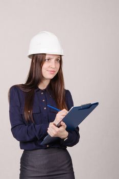 Young woman builder in helmet standing with a folder in hand