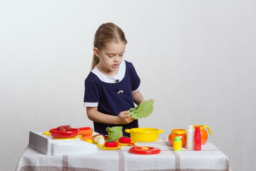Five year old girl playing in a children's mistress dishes at a table covered with a cloth