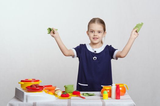 Five year old girl playing in a children's mistress dishes at a table covered with a cloth