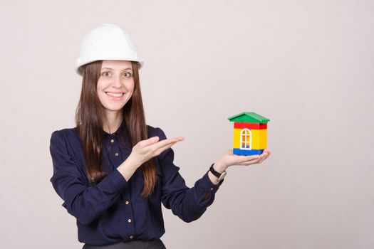 Young woman builder in helmet with a house worth in the hands of