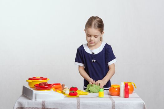 Five year old girl playing in a children's mistress dishes at a table covered with a cloth