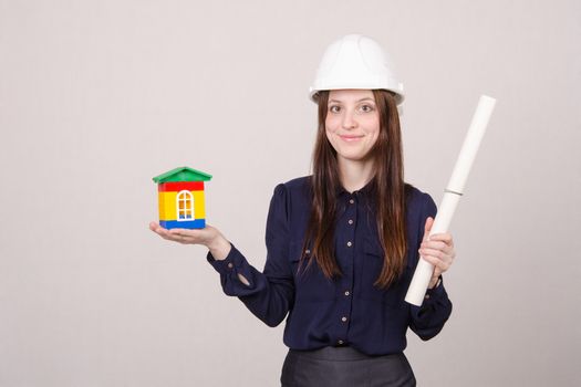 Young woman builder in helmet and with a house worth drawing in the hands of