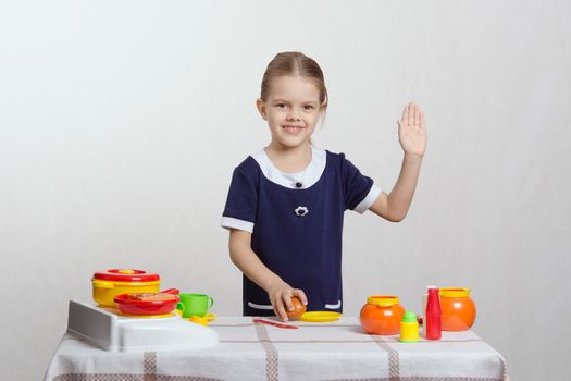 Five year old girl playing in a children's mistress dishes at a table covered with a cloth