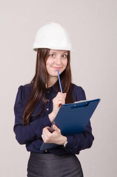 Young woman builder in helmet standing with a folder in hand