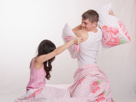 Young couple sitting in bed and beat each other pillows