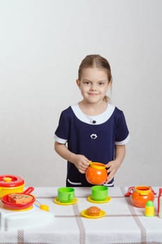 Five year old girl plays children's dishes at a table covered with a cloth