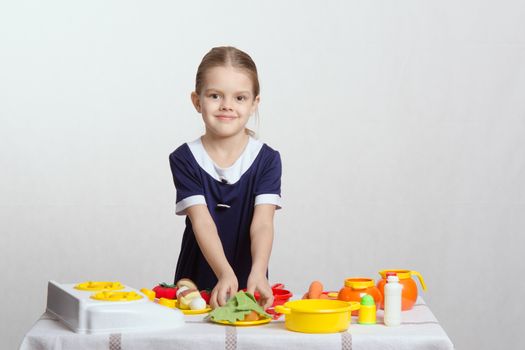 Five year old girl playing in a children's mistress dishes at a table covered with a cloth