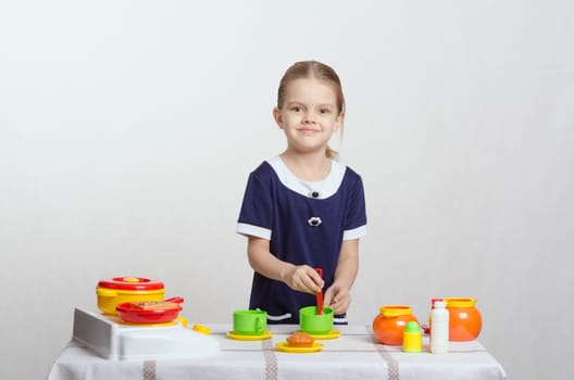 Five year old girl plays children's dishes at a table covered with cloth