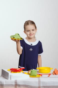 Five year old girl playing in a children's mistress dishes at a table covered with a cloth