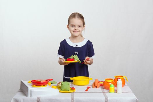 Five year old girl playing in a children's mistress dishes at a table covered with a cloth