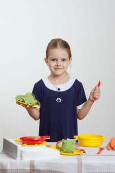 Five year old girl playing in a children's mistress dishes at a table covered with a cloth