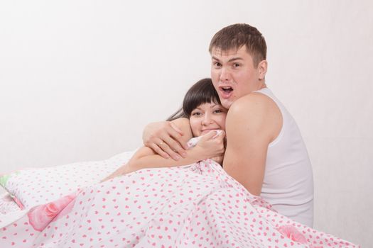 Young beautiful girl and the guy sitting in bed cuddling