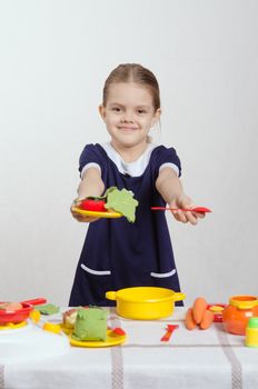 Five year old girl playing in a children's mistress dishes at a table covered with a cloth