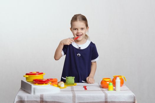Five year old girl playing in a children's mistress dishes at a table covered with a cloth