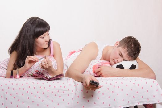 Young girl and a guy in bed. Beautiful girl has a manicure, man watching soccer on TV