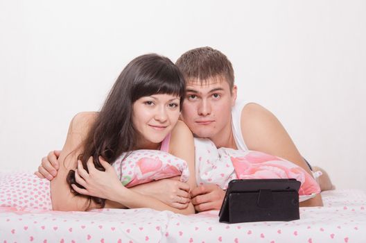 Young beautiful couple watching a movie in the tablet computer while lying in bed