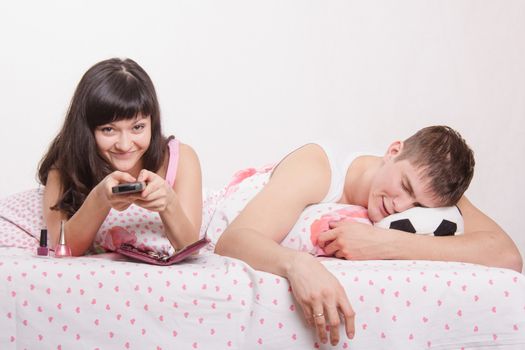 Young girl and a guy in bed. Beautiful girl has manicured nails on the hand, the guy watching soccer on TV