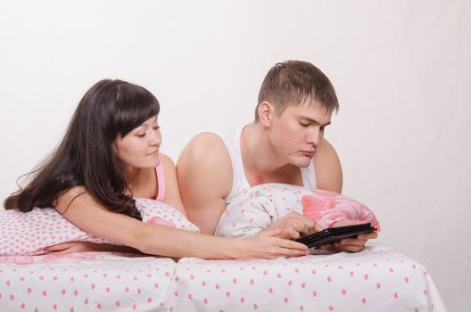 Young beautiful couple watching a movie in the tablet computer while lying in bed