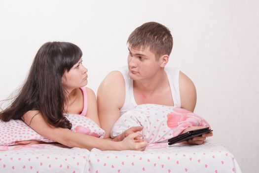 Young beautiful couple watching a movie in the tablet computer while lying in be