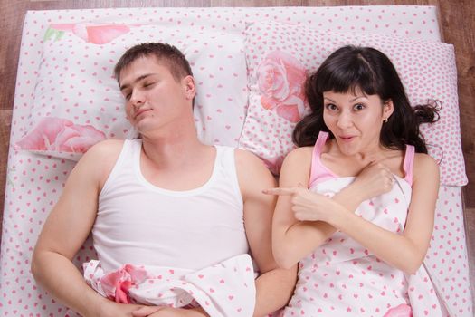 A young girl waking up in the morning sees a stranger guy in bed