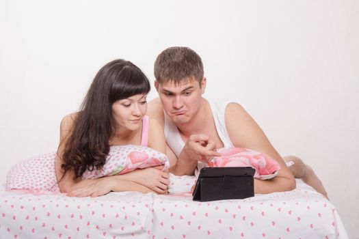 Young beautiful couple watching a movie in the tablet computer while lying in bed