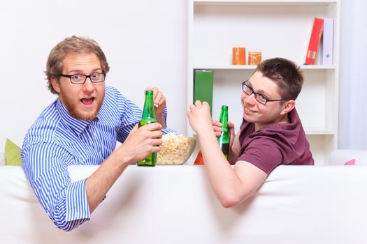 Two guys with beer and popcorn on the sofa during party 