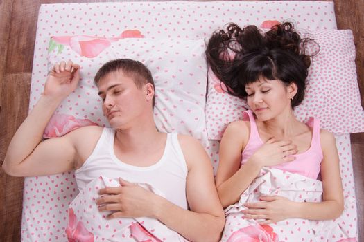 Young beautiful girl looks at the sleeping guy lying in bed