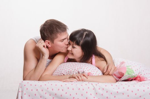 Young beautiful girl and the guy kissing and cuddling in bed