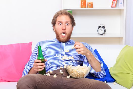 Surprised man eating popcorn on the sofa at home 