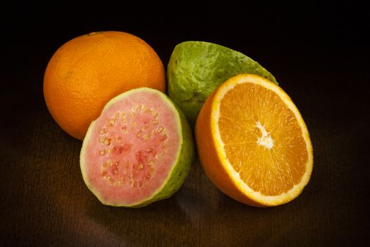 orange and guava cut in half over a table. Dark Background