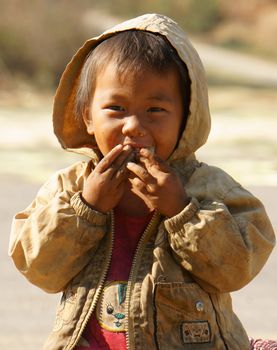 BUON ME THUOT, VIET NAM- FEB 7:Unidentified Asian children sitting on pavement, Vietnamese kid hungry and eating, dirty clothing, barefoot, poverty child at poor countryside, Vietnam, Feb 7, 2014