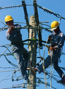 DONG THAP, VIET NAM- SEPT 23: Two Asian electrician climb high in pole to work, lineman with cable network, man repair electric post with belt safety, this is industry service, Vietnam, Sept 23, 2014