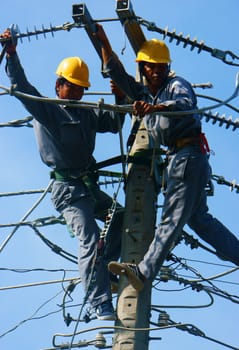 DONG THAP, VIET NAM- SEPT 23: Two Asian electrician climb high in pole to work, lineman with cable network, man repair electric post with belt safety, this is industry service, Vietnam, Sept 23, 2014