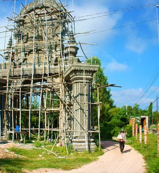 AN GIANG, VIET NAM- SEPT 20: Asian farmer carry tool walking on countryside path, construction work to construct khmer pagoda gate with pattern, development of religion, Vietnam, Sept 20, 2014