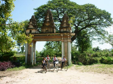 AN GIANG, VIET NAM- SEPT 20: Group of Asian primary pupil riding bike to Khmer village gate, ancient gate with large green tree, big brach make shade, kid happy with friendship, Vietnam, Sept 20, 2014