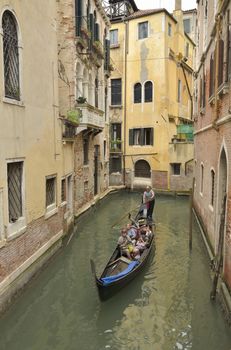 Gondola with tourists crossing a small canal in Venice, Italy