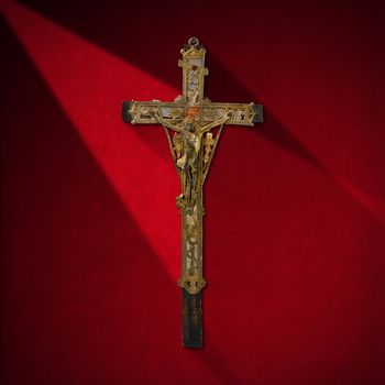 Ancient wooden cross with Jesus in silver on red velvet background with shadows