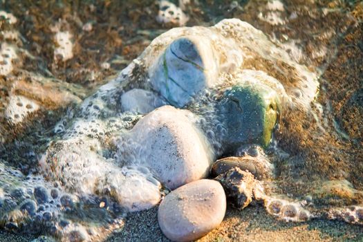 Small multi-colored sea stones on the beach, covered with transparent sea water.