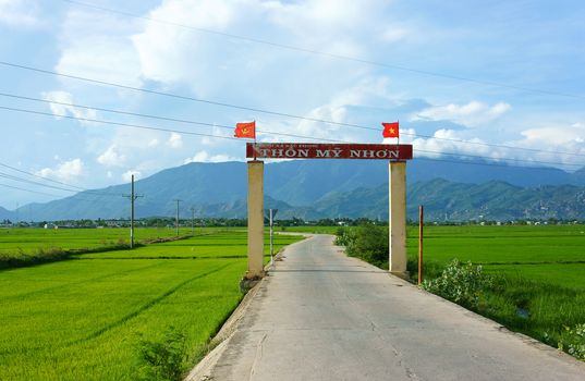 PHAN RANG, VIET NAM- OCT 22: Amazing scenery at Vietnamese countryside, country lane in impression shape, beautiful green rice filed, hamlet gate with flag, mountain under cloud sky, Vietnam, 2014