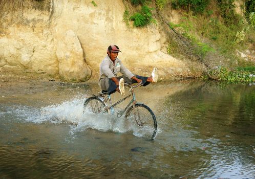 PHAN RANG, VIET NAM- OCT 22: Asian man riding bike cross stream, people across water with stone, lifestyle at poor Vietnamese countryside, this danger and unsafe, Vietnam, Oct 22, 2014