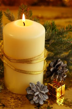 Christmas decorative burning candle, fir branch and decor over golden bokeh background