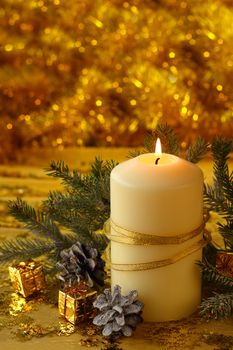 Christmas decorative burning candle, fir branch and decor over golden bokeh background