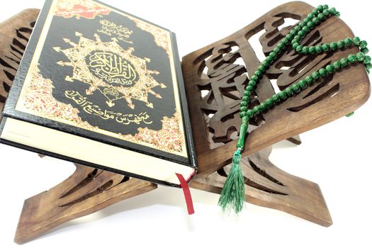 stand with Quran and green rosary before light background