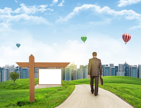 Businessman walks on road. Rear view. City skyline, grass field, wooden signboard and sky in background. Business concept