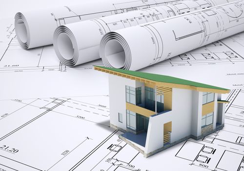 Small model house with green roof near scrolls of architectural drawings. Construction concept