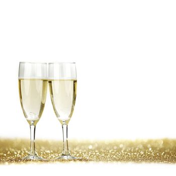 Two champagne glasses and golden shiny glitters isolated on white background