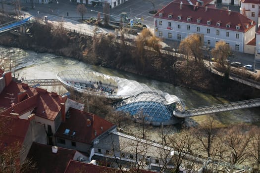 Graz, Austria - January 16, 2011: Island on Mur river connected by a modern steel and glass bridge, Styria, Graz, Austria