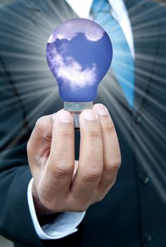 Business man in suit holding a bulb with blue skies and clouds 